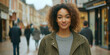 © VALUEINVESTOR - A beautiful mixed-race woman with curly hair, wearing an olive green jacket and a grey shirt underneath, stands on the street of town, generative AI