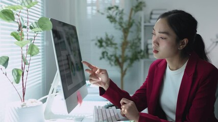 Wall Mural - Young professional woman is working with financial documents and using smartphone while sitting at her workplace with computer in modern office.