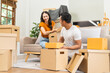 © M+Isolation+Photo - A happy young couple sits on a sofa, packing belongings into boxes, preparing to move to a new house, enjoying teamwork, organizing items, showing excitement, and embracing a fresh start