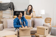 © M+Isolation+Photo - Young couple sitting on a sofa, helping each other pack, collecting clothes, putting items in boxes, feeling happy and excited while preparing to move into their new apartment