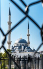 The white stone of the grand BWS shÃ—</ scored with intricate carvings and minarets, seen through black chain link fence in front, clear blue sky, mosque seen from far away, stock photo, 