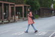 © crizzystudio - Young woman with a backpack is crossing the street on a pedestrian crossing, walking confidently towards her destination near a university campus