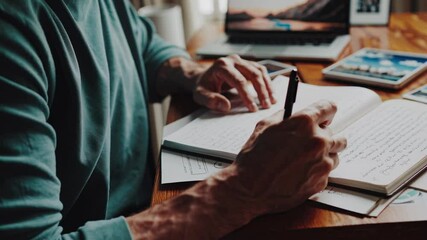 Poster - Person writing in a notebook while working on a laptop at a wooden desk with coffee and phone nearby