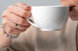 © pavel siamionov - A close-up of a person holding a white cup, sipping a warm beverage. focus is on the hand adorned with a bracelet, conveying a cozy and relaxing atmosphere. Perfect for lifestyle or wellness themes.