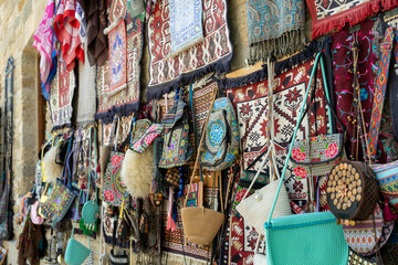 A wall of handbags and purses with a variety of colors and designs. The wall is decorated with rugs and other items