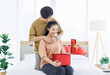© Bangkok Click Studio - Portrait of young lovely sweet romantic asian happy couple love hugging embracing holding gift box presenting for Valentine's day sitting on the bed in bedroom at home smiling enjoy good time together