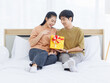 © Bangkok Click Studio - Portrait of young lovely sweet attractive asian happy couple love man giving surprise present gift box to beloved woman for Valentine's day in bedroom at home smiling enjoy good time romantic together