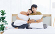 © Bangkok Click Studio - Portrait of young lovely sweet attractive asian happy couple love posing to camera smiling hugging pillow sitting on white bed in bedroom at home good time romantic together Valentine's day concept.