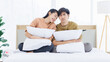 © Bangkok Click Studio - Portrait of young lovely sweet attractive asian happy couple love posing to camera smiling hugging pillow sitting on white bed in bedroom at home good time romantic together Valentine's day concept.