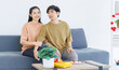 © Bangkok Click Studio - Asian young happy attractive couple love sweethearts smile hugging embracing cuddle sitting on cozy sofa in living room at home to celebrating anniversary surprise enjoy good time together.