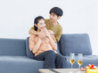 © Bangkok Click Studio - Asian young happy attractive couple love sweethearts smile hugging embracing cuddle sitting on cozy sofa in living room at home to celebrating anniversary surprise enjoy good time together.
