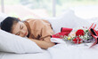 © Bangkok Click Studio - Portrait of asian young beautiful woman sleeping and dreaming on a white bed with a bouquet of red roses that boyfriend give in a special day Valentine's day in the bedroom at home happy good time.