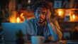 © ezen - Stressed man working late on laptop, home office, warm lighting