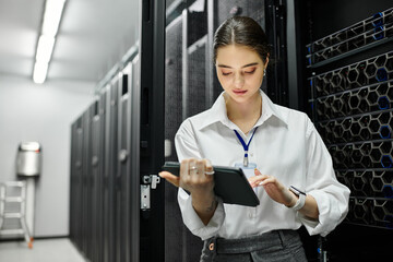 A woman in a white shirt supervises server operations using a tablet in a data center.
