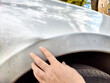 © keleny - A hand carefully examines a dent on the side of a silver vehicle under clear skies near apartments