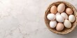 © ShStock - Basket filled with assorted chicken eggs on a light marble background top down view with ample copy space on the left side of the image