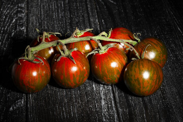 Wall Mural - kumato cherry tomato branch on black wood background