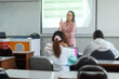 © EduLife Photos - A lecturer stands at the front of the classroom, engaging students with a presentation projected on the screen. The students sit at desks, focused on the lecture.