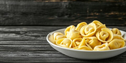 Poster - Delicious tortellini pasta elegantly arranged in a white bowl on a dark wooden table with a textured backdrop and space for text on the right side