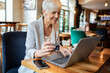 © Davor - Senior businesswoman enjoying coffee while working on laptop at cafe