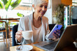 © Davor - Senior businesswoman enjoying coffee while working on laptop at cafe