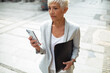 © Davor - Senior professional businesswoman using smartphone downtown