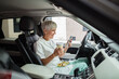 © Davor - Senior nurse eating salad on break in car and using smartphone