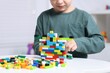 © New Africa - Cute boy playing with building blocks at white table indoors, closeup