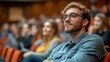 © Darni - Young man attentively listening to a lecture in a crowded auditorium.