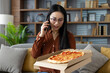 © Liubomir - Asian woman enjoying pizza delivery on couch, talking on phone, feeling relaxed in home atmosphere. Experience blends delicious comfort food with modern communication in cozy setting.