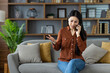 © Liubomir - Concerned asian woman using smartphone, sitting on sofa, discussing important issue. Displays emotion, communication, technology in modern living room setting.