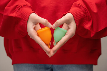 Wall Mural - Young woman holding menstrual cups in the shape of a heart on a red background, close-up