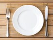 © WE.ARE.AI - Blank Plate Mockup. A minimalist dining setup featuring a white plate, fork, and knife on a wooden table with a bamboo mat.