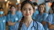 © mankjon - Portrait of a Young Asian Female Medical Professional with a Braided Hairstyle, Smiling Confidently in a Busy Hospital Setting