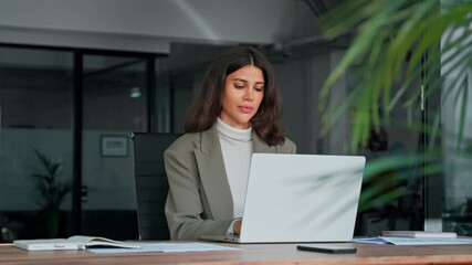 Young professional it specialist latin hispanic business lady working on laptop pc sitting at desk in modern office space. 30s middle eastern indian woman using computer technology app for work online