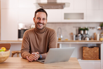 Wall Mural - positive male entrepreneur with computer on dining table smiling at camera while working from home