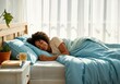 © Jenny - African female adult sleeping in cozy bed with blue bedding and natural light
