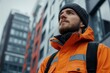 © Haroshka - Young man wearing an orange jacket and beanie observes the urban landscape on a cool, overcast day