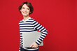 © ViDi Studio - Side view young happy IT woman wear blue striped sweatshirt casual clothes hold use work on laptop pc computer look aside on area isolated on plain red background studio portrait. Lifestyle concept.