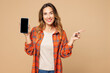 © ViDi Studio - Young woman wear orange shirt casual clothes hold in hand use mobile cell phone with blank screen workspace area point finger aside isolated on plain pastel light beige background. Lifestyle concept.