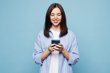 Wall Mural - Young smiling Caucasian woman she wears shirt casual clothes hold in hand use mobile cell phone chatting online isolated on plain pastel light blue cyan background studio portrait. Lifestyle concept.