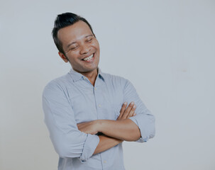 Wall Mural - Asian man wearing light blue shirt smiling with closed eye and arms crossed, isolated on white background.