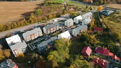 Wall Mural - Modern residential buildings near vibrant autumn forest, aerial view. Contemporary apartments in suburban eco friendly neighborhood with green spaces near mountains in small European town