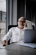 © Lev Lievin - An older gray-haired businessman with glasses sits at his desk, engaged in a business conversation on the phone. Professional, confident, and focused on work.
