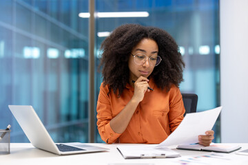 Thinking woman financier reading report, businesswoman holding document in hands. Office worker accountant doing paperwork inside office with laptop.