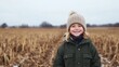 © Sergey - A happy child in a warm jacket and knitted hat smiles while standing in a harvested pumpkin field on a cloudy day.