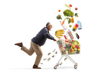 Wall Mural - Excited mature man running with money and falling food in a shopping cart