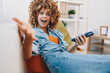 © SHOTPRIME STUDIO - Smiling woman holding mobile phone, enjoying relaxation and entertainment on cozy sofa at home.