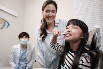 Wall Mural - An Asian girl demonstrates teeth brushing to mother and pediatric dentist with toothbrush in dental clinic with happy smile, mouth dentistry hygiene, and orthodontic healthcare work in kid hospital.