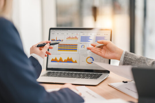 Business professionals analyzing financial data and charts on laptop during meeting, discussing strategies and performance metrics in modern office setting